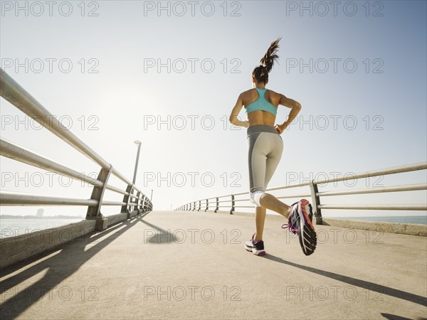 Rear view of woman jogging on bridge on sunny day