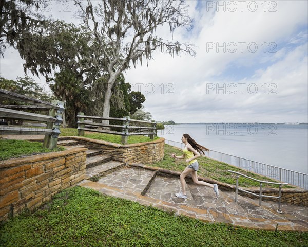 Athlete woman running up steps by river