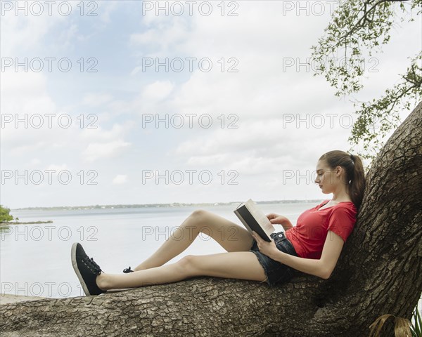 Woman sitting on tree and reading book