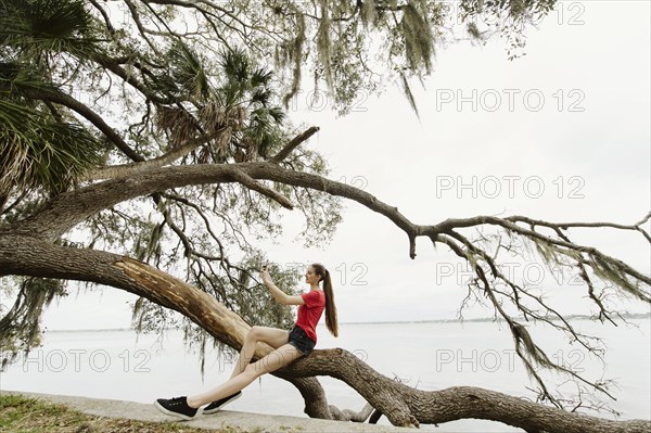 Woman taking selfie on tree branch by river