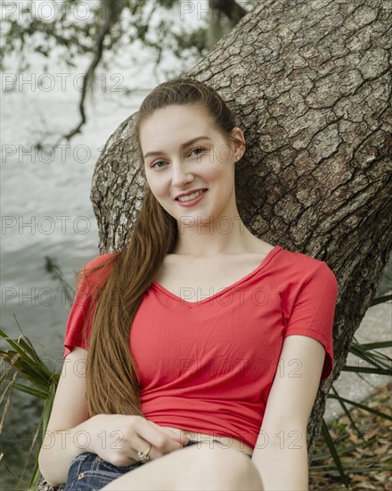 Portrait of smiling woman leaning against tree trunk