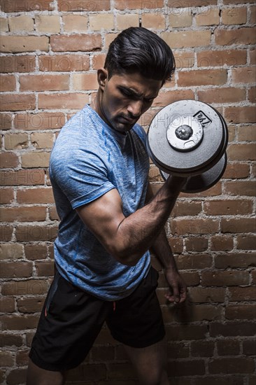 Man exercising with dumbbell against brick wall