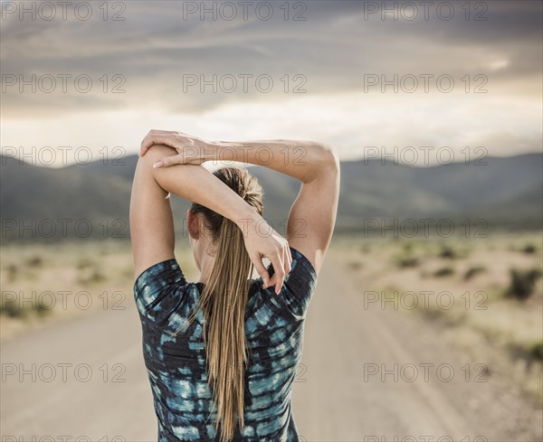 Rear view of woman stretching on road in desert landscape