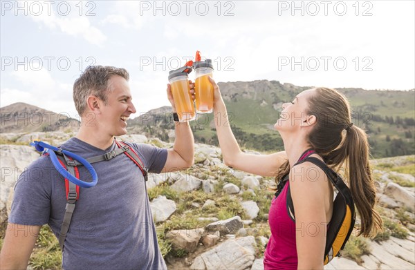 Smiling hiking couple raising toast with energy drinks