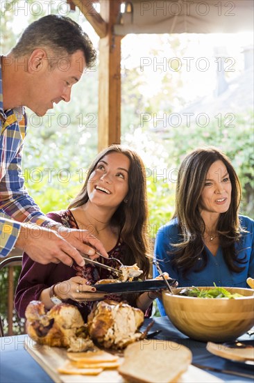 Man serving roasted turkey to smiling woman at dining table