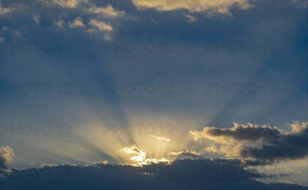 Sun rays streaking upwards from clouds against sky