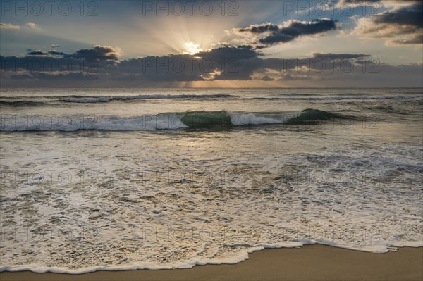 Rising sun shining through clouds above ocean