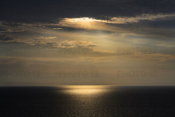 Sun shining through storm clouds and reflecting in ocean surface