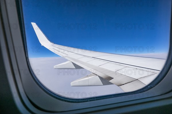 Airplane wing seen against blue sky through airplane window