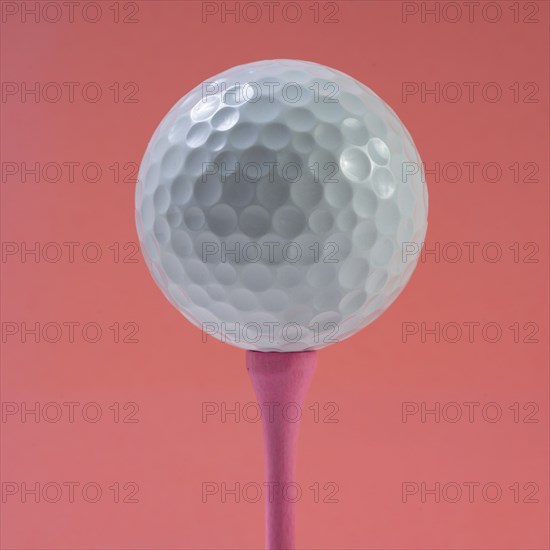 Golf ball on tee against pink background