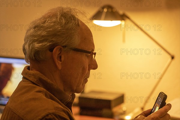 Profile of senior man using smart phone at desk