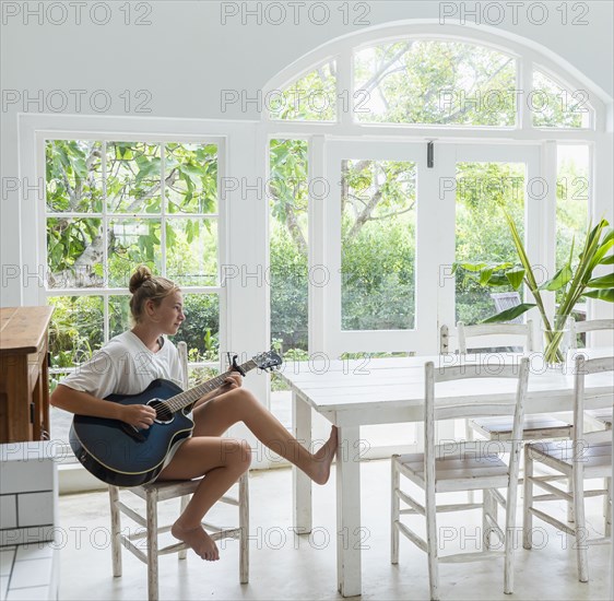 Teenage girl (16-17) playing guitar in white room