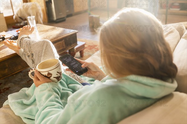 Teenage girl (16-17) with smartphone resting on sofa