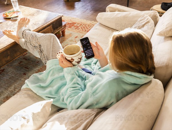 Teenage girl (16-17) with smartphone resting on sofa