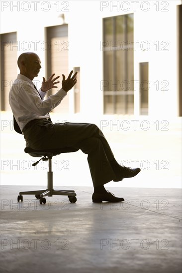 Businessman in warehouse sitting on office chair and gesturing