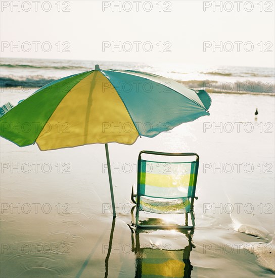 Beach chair and umbrella on beach at sunset