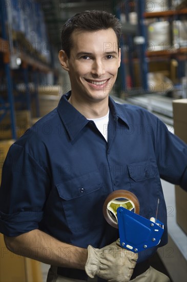 Portrait of man holding tape gun in warehouse