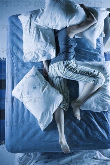 Woman sleeping in bed with pillow over head