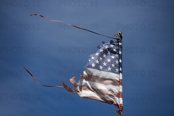 Worn and wind-torn American flag blowing against blue sky