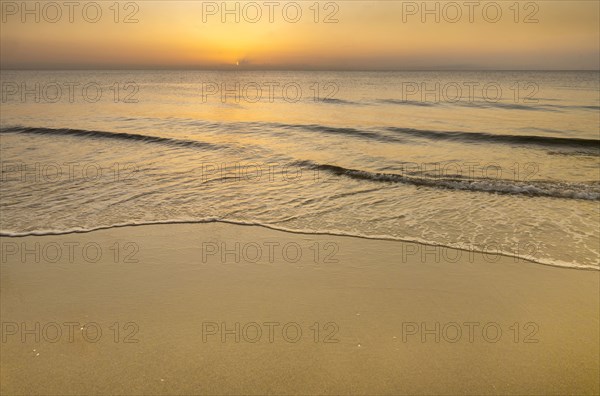 Calm ocean surf washing up onto beach at sunrise