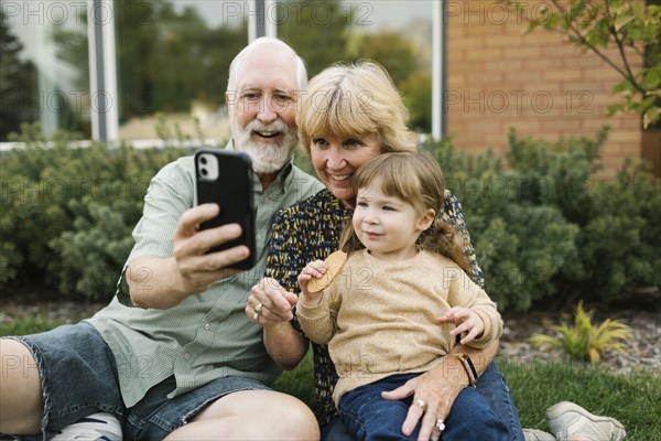 Smiling grandparents taking selfie with granddaughter