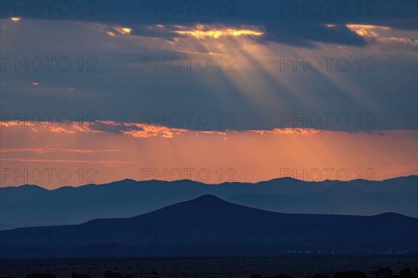 Sunbeams shining through storm clouds over mountains at sunset