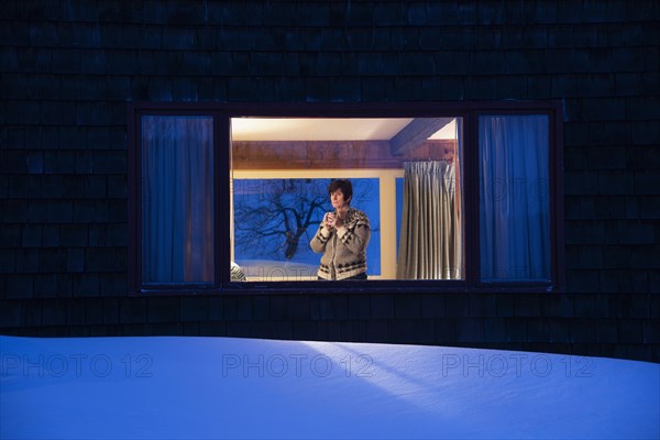 Woman looking through window at dusk in winter