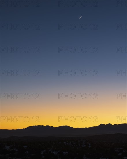 Jemez Mountains at dusk with crescent moon on sky