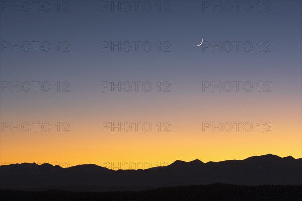 Jemez Mountains at dusk with crescent moon on sky