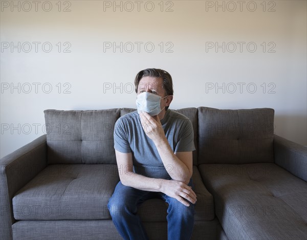 Pensive man in face mask sitting on sofa