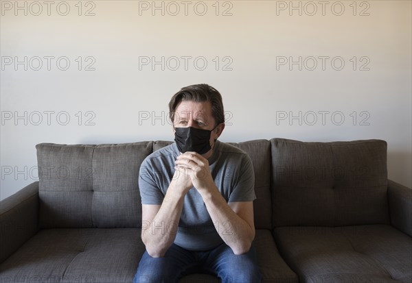 Pensive man in face mask sitting on sofa