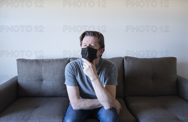 Pensive man in face mask sitting on sofa