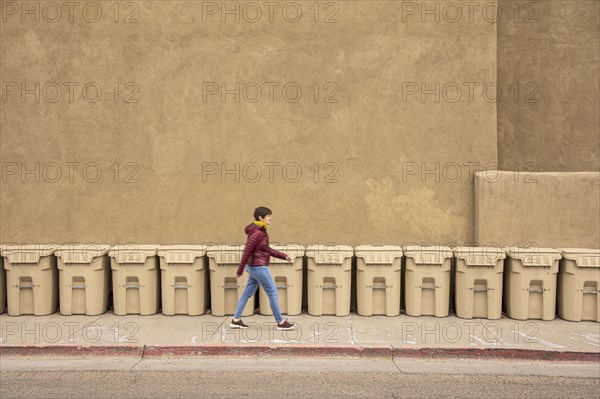 USA, New Mexico, Santa Fe, Woman walking past row of garbage bins