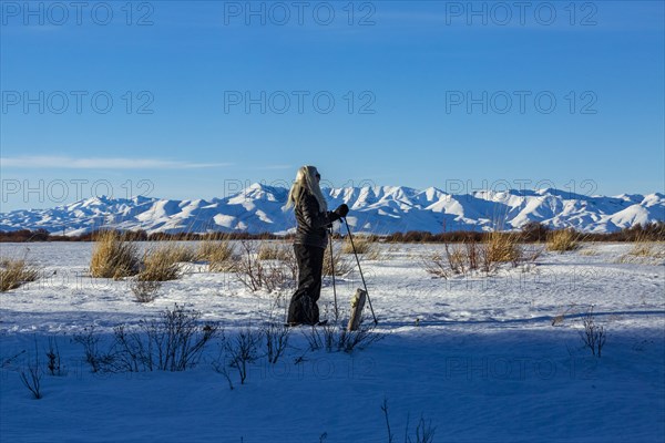 Senior blonde woman snow shoeing in snow covered landscape