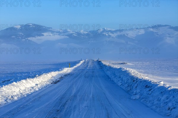 Snow covered rural road leading to mountains