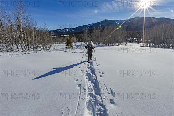 Rear view of senior blonde woman snow shoeing in snow covered landscape
