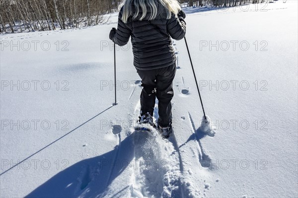 Rear view of senior woman snow shoeing in snow covered field