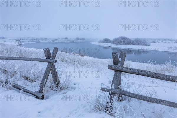 Wooden fence in snow covered field near river