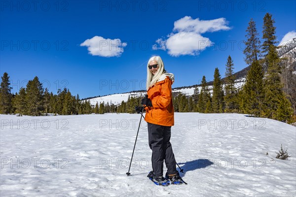 Senior blonde woman snow shoeing in snow covered landscape