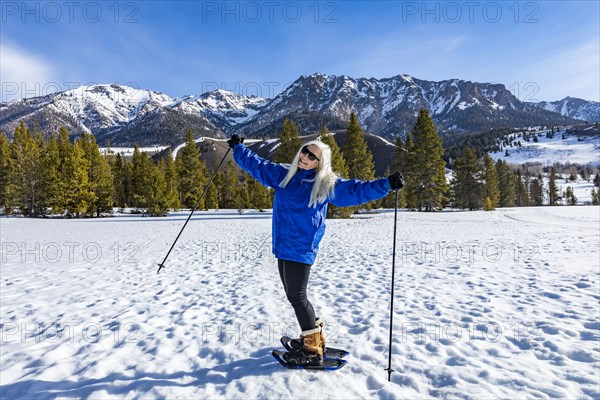 Portrait of smiling senior blonde woman with snowshoes in landscape