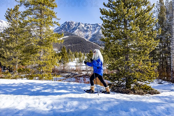 Senior blonde woman snowshoeing in snow covered landscape