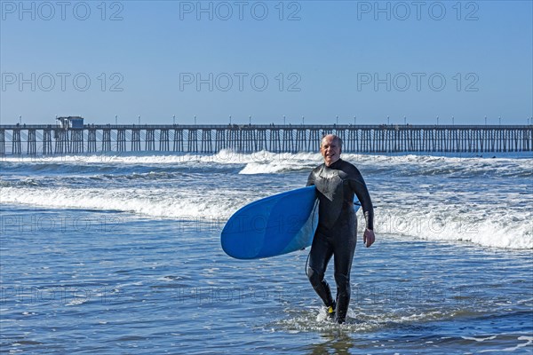 USA, California, Oceanside, Senior surfer carrying surfboard