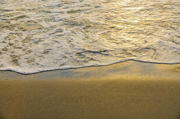 Close-up of calm ocean surf washing up onto beach at sunset