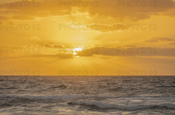 Golden sky with sun and calm ocean at sunset