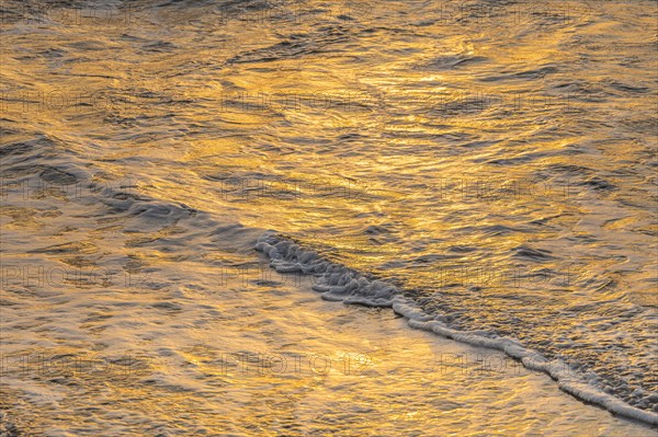 Close-up of calm ocean surf washing up onto beach at sunset
