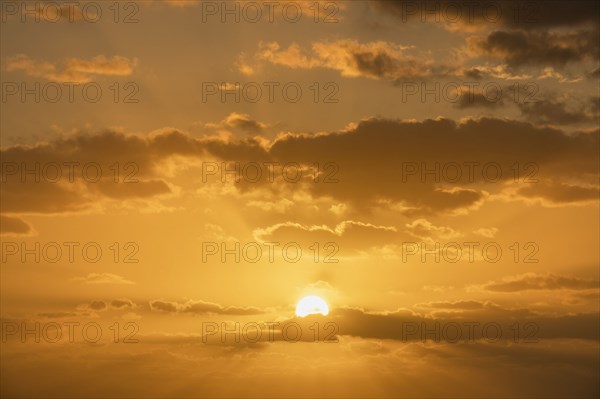 Golden sunrise sky with cumulus clouds and sun