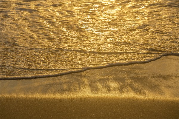 Close-up of calm ocean surf washing up onto beach at sunset