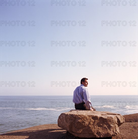 USA, California, Point Mugu, Businessman sitting on rock on beach