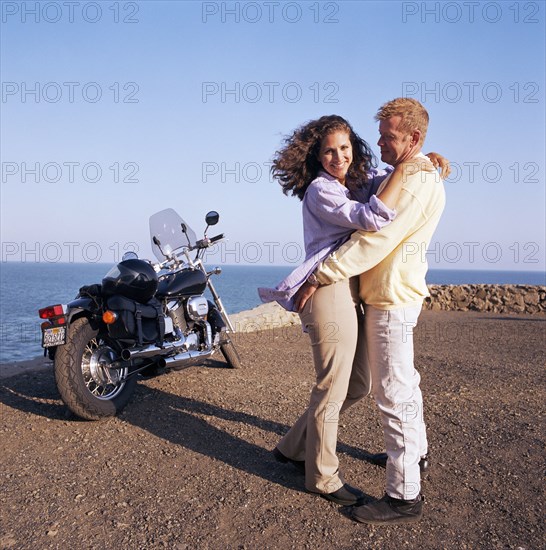 USA, California, Point Mugu, Couple hugging on coast next to motorcycle