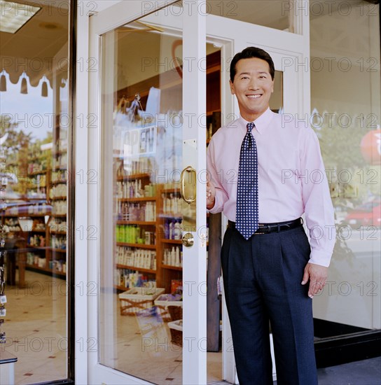 Portrait of store owner opening door to pharmacy